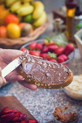 Young women spreading chocolate cream on bread, while preparing healthy sweet toast for the breakfast