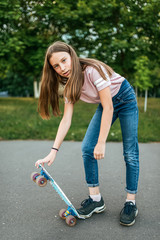 Girl teenager 9-11 years old, riding a skateboard. In the summer in the city in casual jeans and sneakers.
