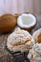 Delicious homemade coconut meringue type biscuits next to chopped coconut and coconut chips on a wooden table