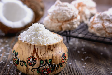 Coconut chips in a wooden vessel on a background of chopped coconut and cookies on a wooden table