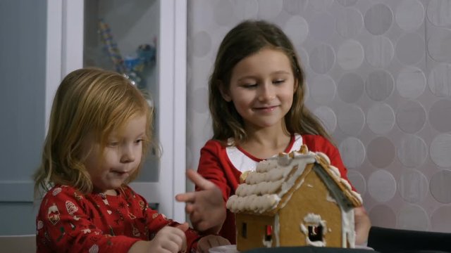 Kids eating an gingerbread house, two little girls sitting and eating sweets
