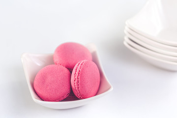 Several sweet tasty pink macarons in a pile of small white bowls with copy space closeup