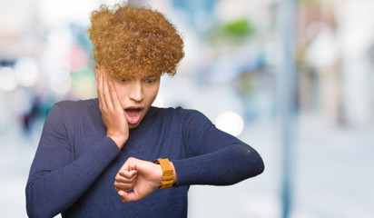 Young handsome man with afro hair Looking at the watch time worried, afraid of getting late