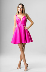 Full body young woman wearing a purple dress posing on a grey background