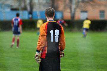 A goalkeeper is standing and looking at his team playing the game. 