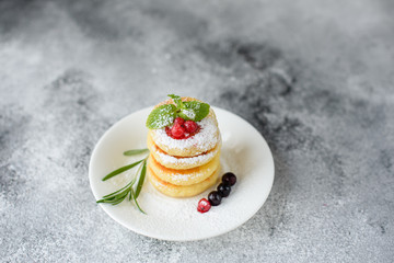 Tasty fresh cottage cheese pancakes on a white plate with a glass of milk on a concrete background. Healthy and diet breakfast