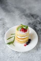Tasty fresh cottage cheese pancakes on a white plate with a glass of milk on a concrete background. Healthy and diet breakfast