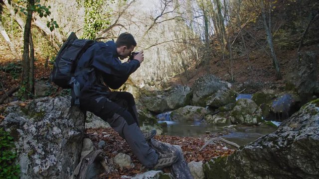 Man taking a picture of a small waterfall in the forest. 4k