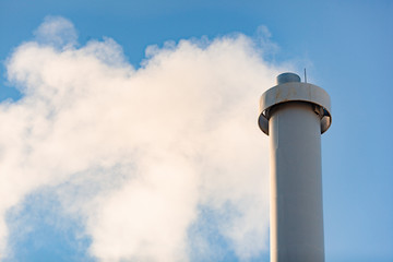 Industrial building with one high grey chimney with smoke. background on blue sky
