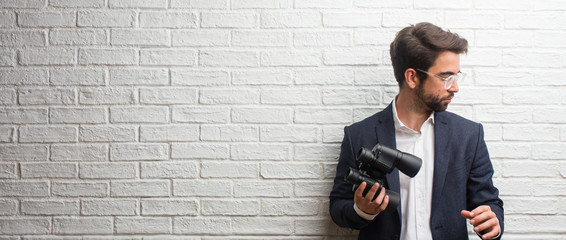 Young business man wearing a suit against a white bricks wall surprised and shocked, looking with wide eyes, excited by an offer or by a new job, win concept