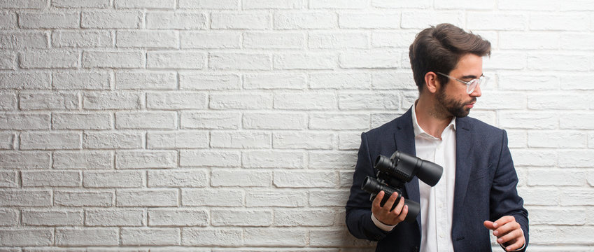 Young business man wearing a suit against a white bricks wall surprised and shocked, looking with wide eyes, excited by an offer or by a new job, win concept