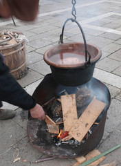 elderly man puts pieces of wood on the bonfire with a copper cau