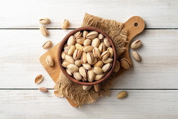 Salted pistachio nuts in ceramic bowl on white wooden background. Top view.