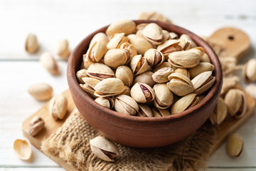 Salted pistachio nuts in ceramic bowl on white wooden background. Selective focus.