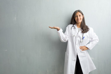 Young indian doctor woman against a wall holding something with hands, showing a product, smiling...