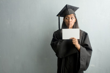 Young graduated indian woman against a wall keeping a secret or asking for silence, serious face, obedience concept. Holding a placard.