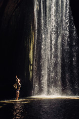 girl standing in the sunlight in a cave with a waterfall