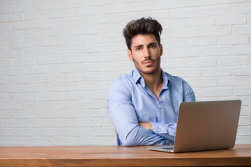 Young business man sitting and working on a laptop crossing his arms, serious and imposing, feeling confident and showing power