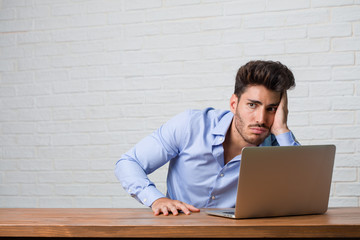 Young business man sitting and working on a laptop frustrated and desperate, angry and sad with hands on head