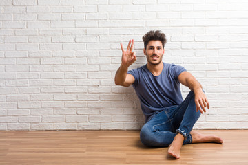 Young natural man sit on a wooden floor showing number three, symbol of counting, concept of mathematics, confident and cheerful