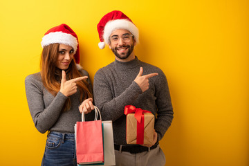 Couple or friends holding gifts and shopping bags pointing to the side with finger
