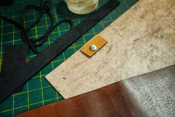 Leatherworking tools. Riveter, awl, ruler, pliers, tassels, pencil, leather pieces, rivets and fasteners are on the table. Close up photo.