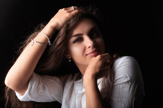 Very pretty young woman with caramel skin. The girl looking at camera and smiling. Model tuching her hair and left sholder. Portrait of pretty young woman with long curly wavy brown hair