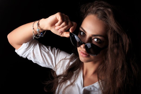 Woman lowering sunglasses and looking at camera. Portrait of pretty young woman with long curly wavy brown hair 