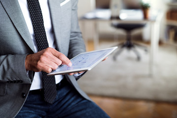 A midsection of businessman sitting in an office, using tablet. Copy space.