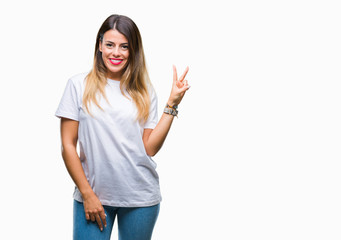 Young beautiful woman casual white t-shirt over isolated background smiling with happy face winking at the camera doing victory sign. Number two.