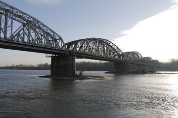 Naklejka premium The Ernest Malinowski Bridge in Torun. Railway bridge on the Vistula river. Visible spans, steel trusses, supports, water current. A winter, cold, windy day. A shore with trees in the background.