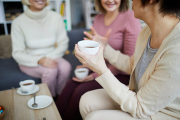 Closeup of unrecognizable businesswoman holding cup of tea while chatting actively with friends, copy space