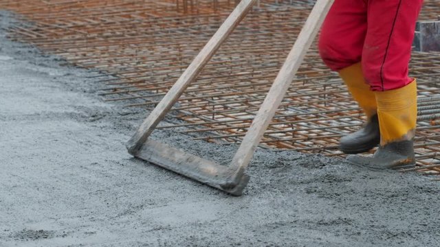 Video of an unrecognised worker levelling concrete with a rake on a construction site