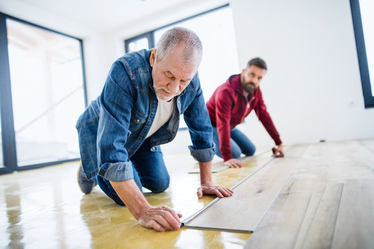 A mature man with his senior father laying vinyl flooring, a new home concept.