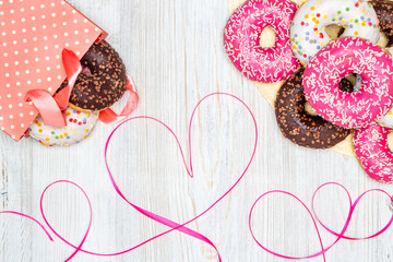 Donuts, gift bag with donuts inside and red ribbon heart on wooden table. Flat lay. Valentine's Day celebration concept