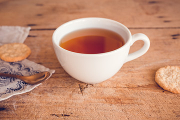 Tee in weißer Tasse auf Holztisch mit Geschirrtuch und kupferfarbenen Löffel