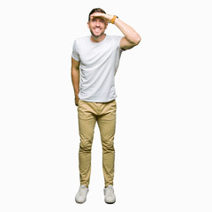 Handsome man wearing casual white t-shirt very happy and smiling looking far away with hand over head. Searching concept.