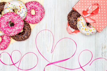 Donuts, gift bag with donuts inside and red ribbon heart on wooden table. Flat lay. Valentine's Day celebration concept
