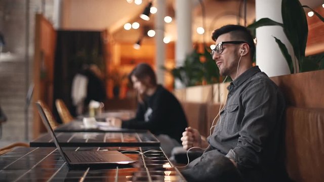 Entrepreneur man in the gray shirt wearing glasses and headphones having break in his work, he enjoying of his favorite songs and singing it in the loft cafe interior