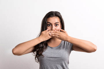 Young beautiful woman standing in a studio in studio, covering mouth with hands.