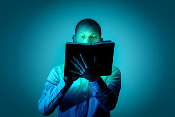 Man is fascinated by reading an exciting book and is illuminated by a magical light