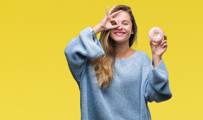 Young beautiful blonde woman eating sweet donut over isolated background with happy face smiling doing ok sign with hand on eye looking through fingers