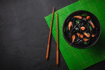 Black squid ink Fettuccine pasta with prawns or shrimps , parsley, chili in wine and butter sauce. Top view on granite with copy space.