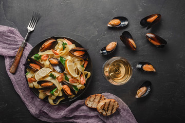 Spaghetti vongole, Italian seafood pasta with clams and mussels, in plate with herbs and glass of white wine on rustic stone background. Traditional Italian sea cuisine, close-up, top view