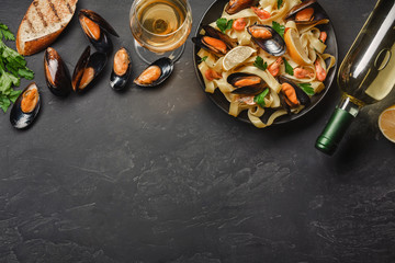 Spaghetti vongole, Italian seafood pasta with clams and mussels, in plate with herbs and bottle of white wine on rustic stone background. Traditional Italian sea cuisine, close-up, top view