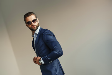 Obraz premium Handsome businessman at office. Bearded sexy man in a stylish suit and sunglasses is standing at office and looking away