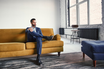 Feeling relaxed...Handsome and stylish young businessman is resting on sofa and thinking about business ideas