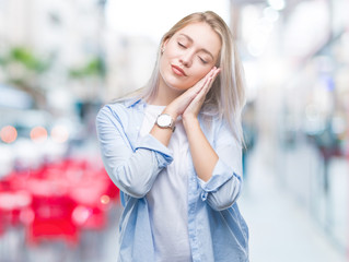 Young blonde woman over isolated background sleeping tired dreaming and posing with hands together while smiling with closed eyes.