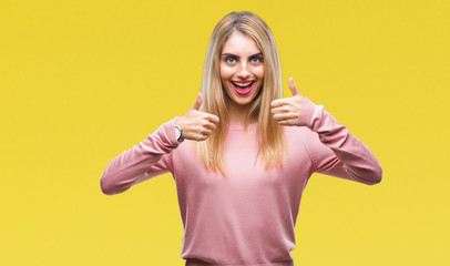 Young beautiful blonde woman wearing pink winter sweater over isolated background success sign doing positive gesture with hand, thumbs up smiling and happy. Looking at the camera