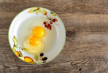 Raw egg yolks in the plate isolated on old wooden background, top view.